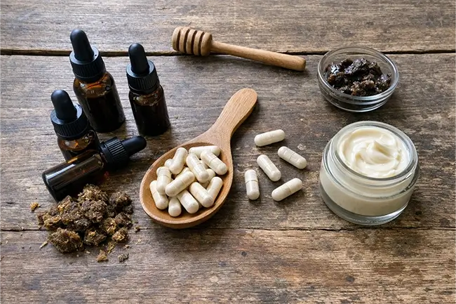 Propolis kopen: diverse producten zoals capsules, druppels en crème op een houten tafel met bijenkorf op de achtergrond