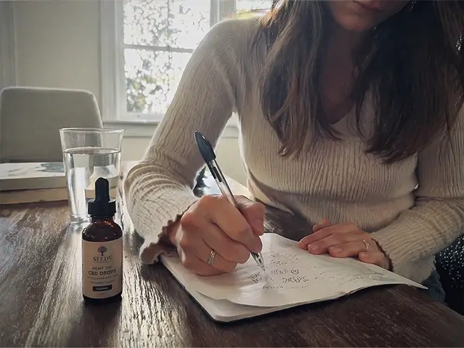 Persoon noteert CBD olie dosering in een dagboek naast een flesje CBD olie