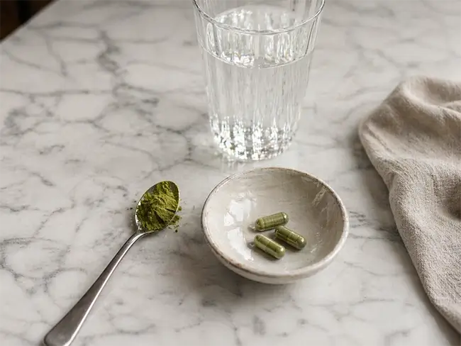 Bladpoeder in theelepel naast capsules en glas water op aanrecht
