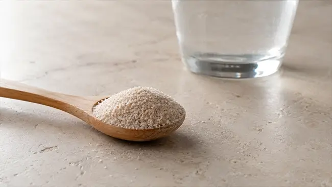 Psyllium husk poeder op een houten lepel naast glas water