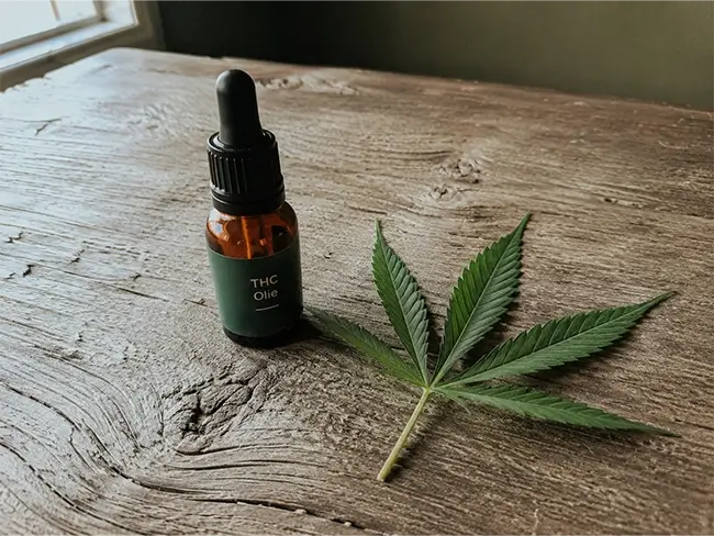 THC olie druppelaar naast hennepblad op houten tafel