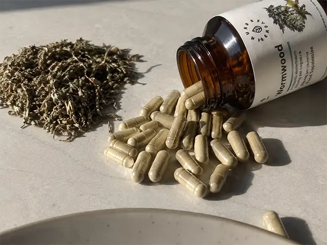 Wormwood capsules met alsemkruid naast een potje op een lichte achtergrond